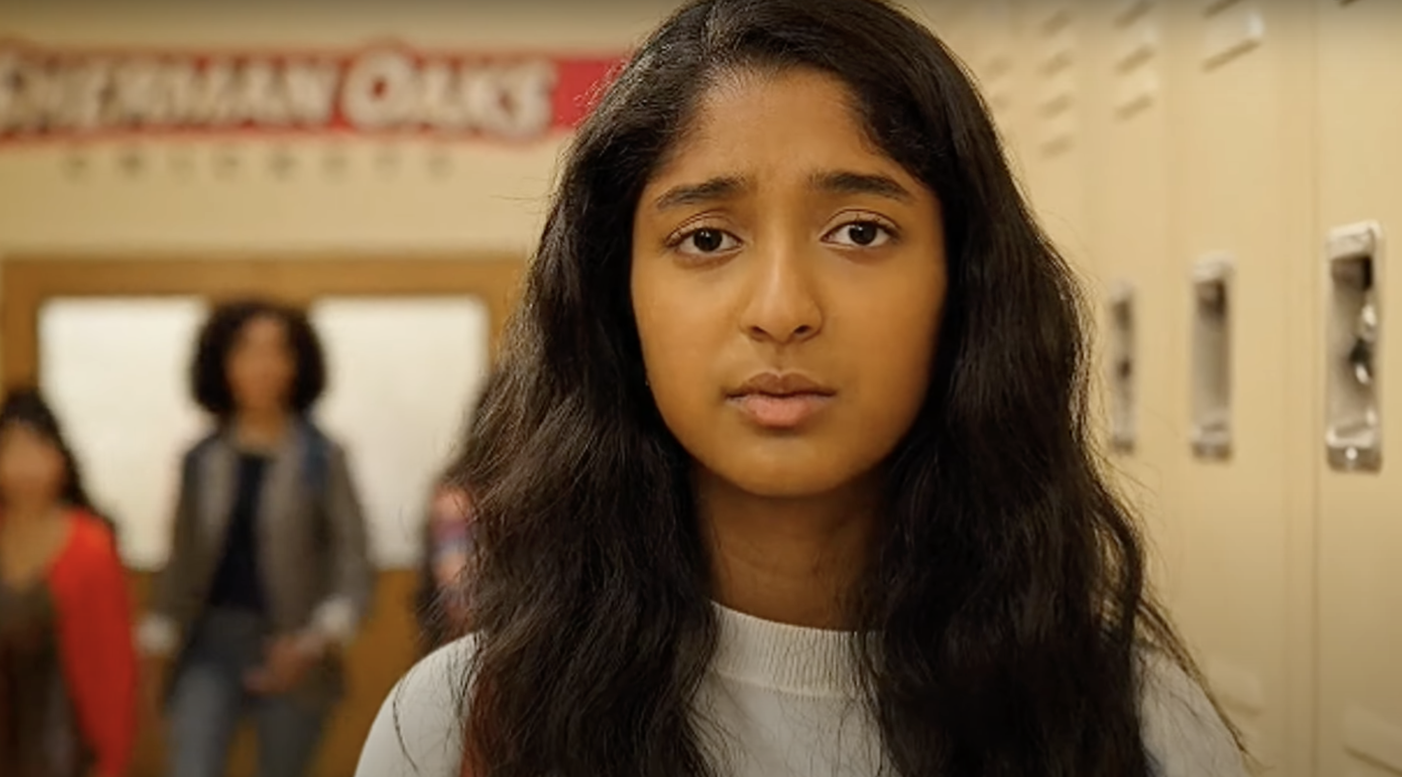 Devi from "Never Have I Ever" looking off into the distance during school