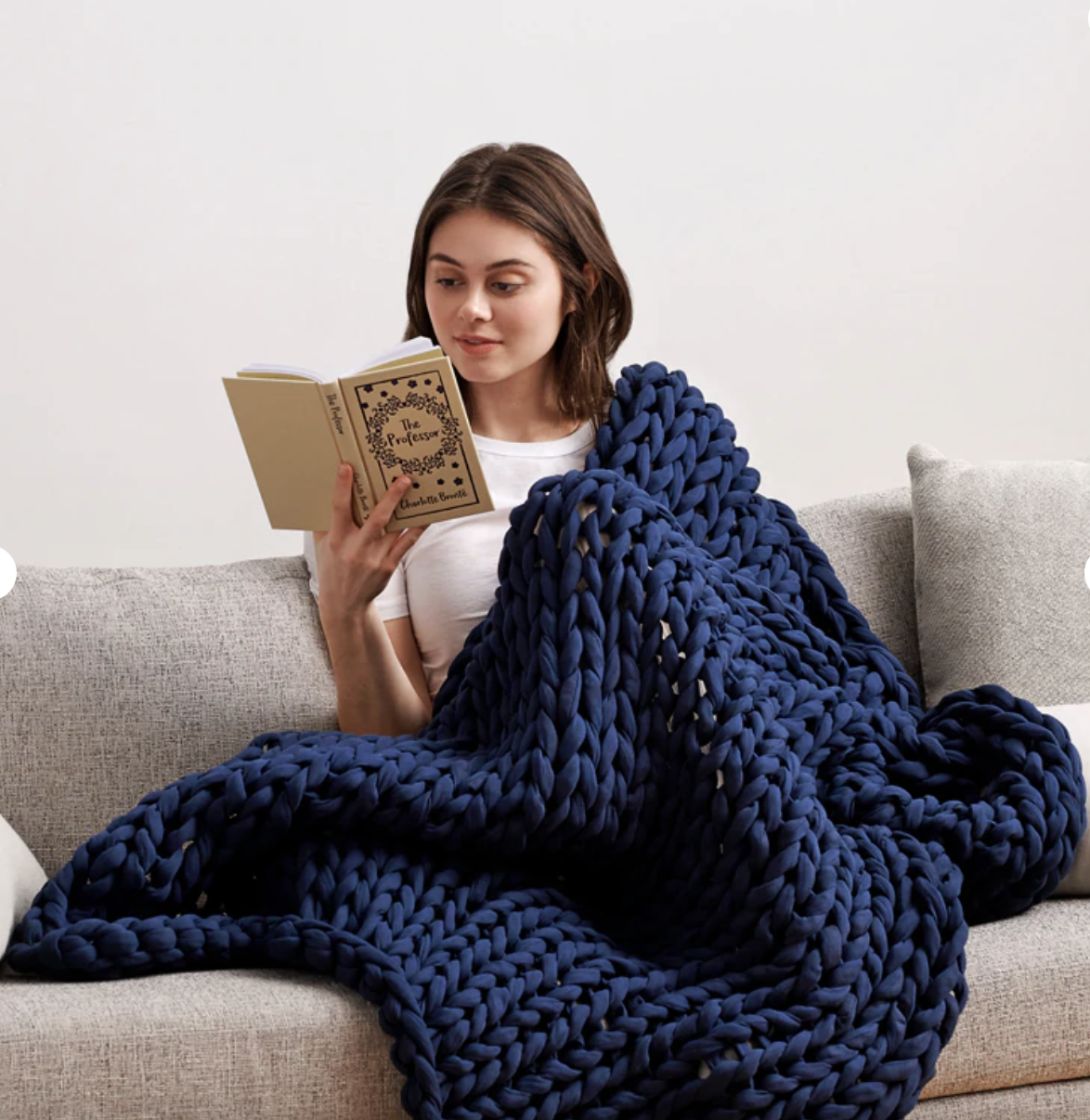 Model reading a book with a navy chunk knitted blanket draped over them
