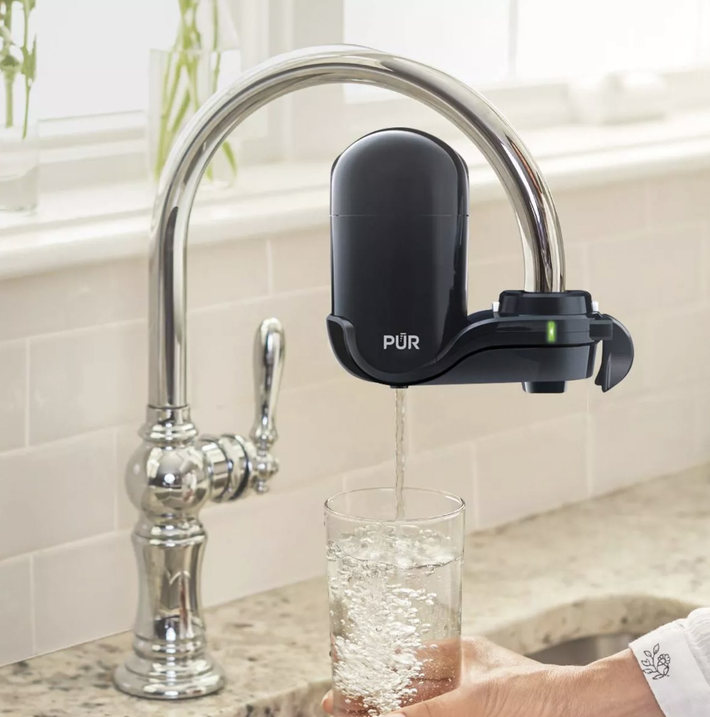 The black filter attached to faucet and dispensing clear purified water into a glass
