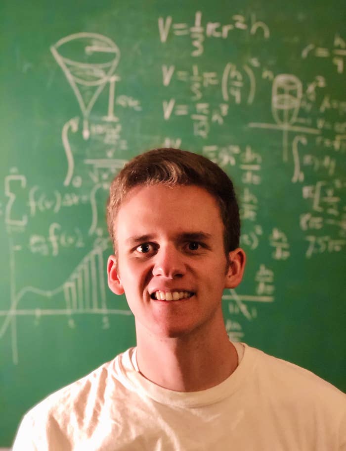 A young man in front of a chalkboard with science equations written on it