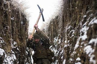 A soldier using a pickax to dig a trench in the snow
