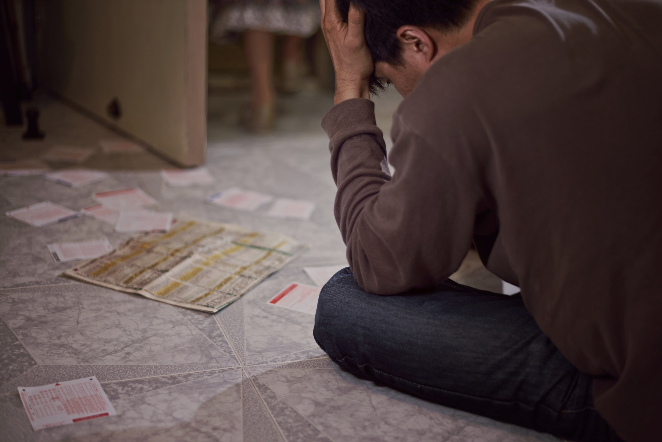 Someone sits on the floor devastated, surrounded by lottery tickets