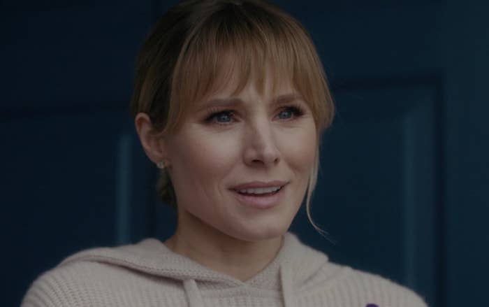 Kristen Bell with bangs and her hair pulled answering her front door