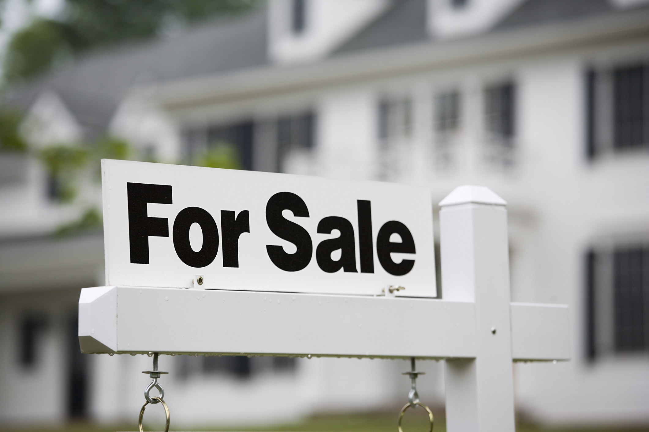 A &quot;For Sale&quot; sign in front of a large house
