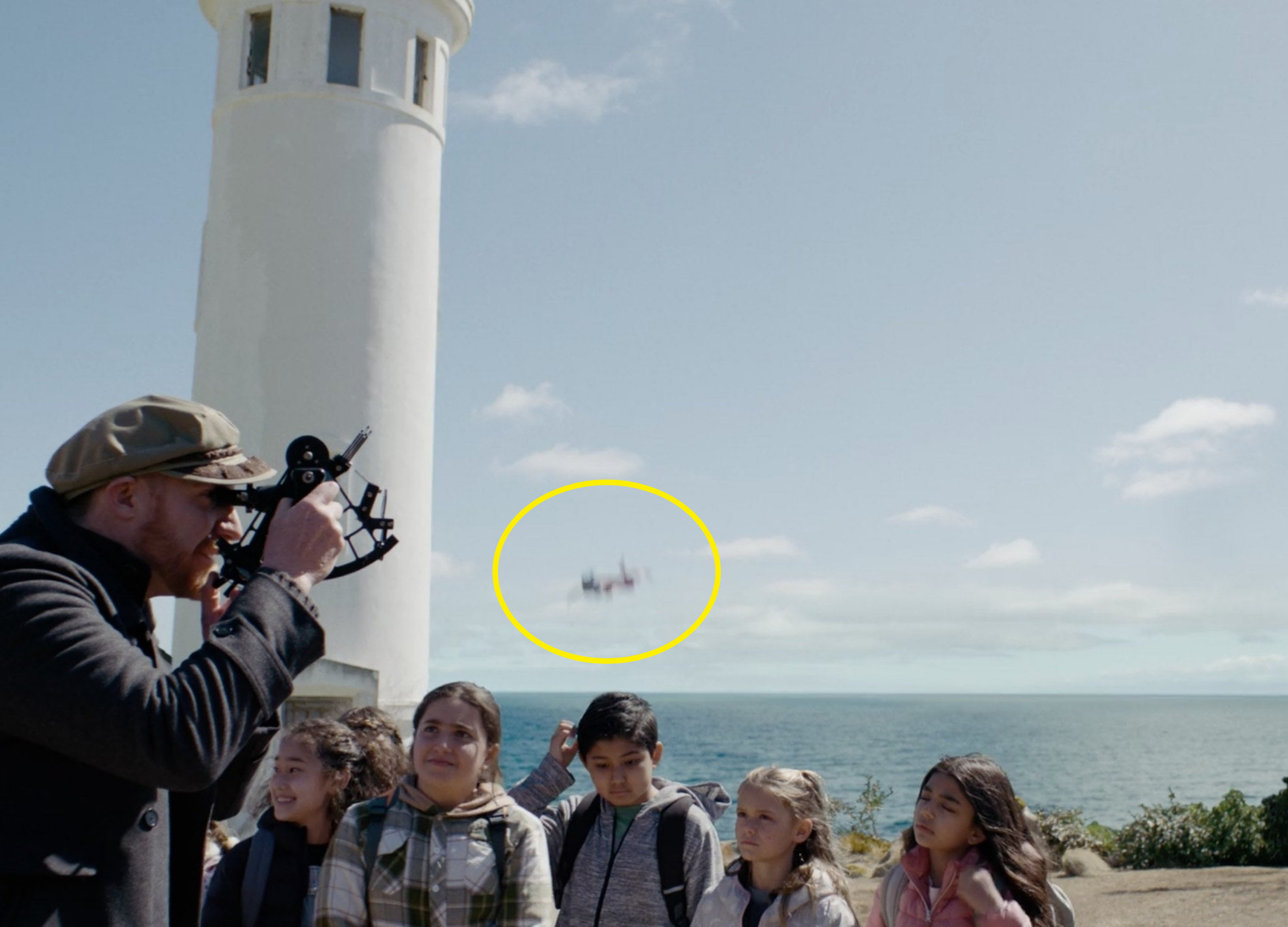 A lighthouse keeper showing off equipment to a group of school children while their teacher falls from a lighthouse to her death in the background
