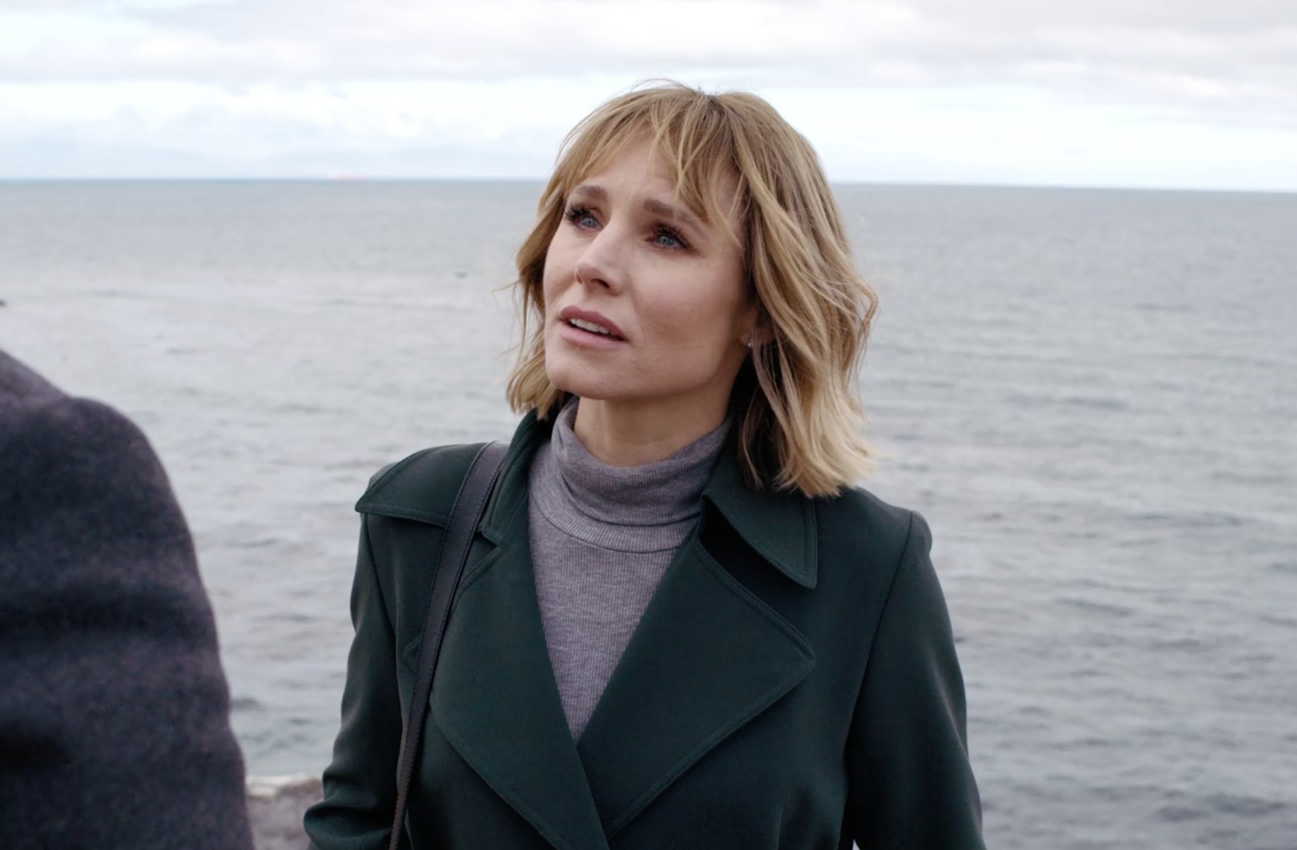 Kristen Bell in front of the ocean looking at someone with a sad expression on her face