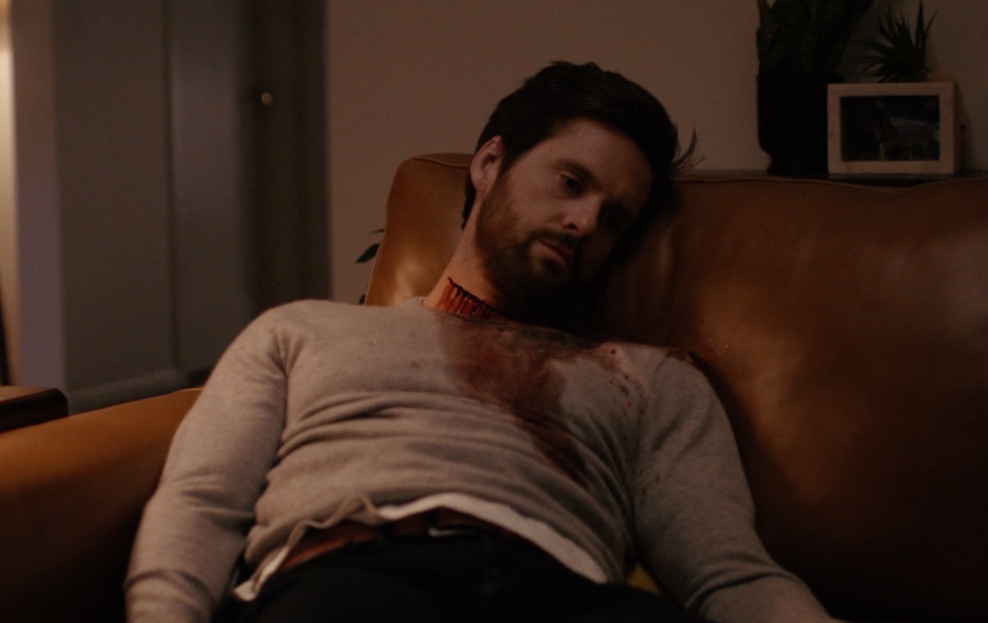Neil slumped on a leather couch bleeding from his cut throat, clearly deceased