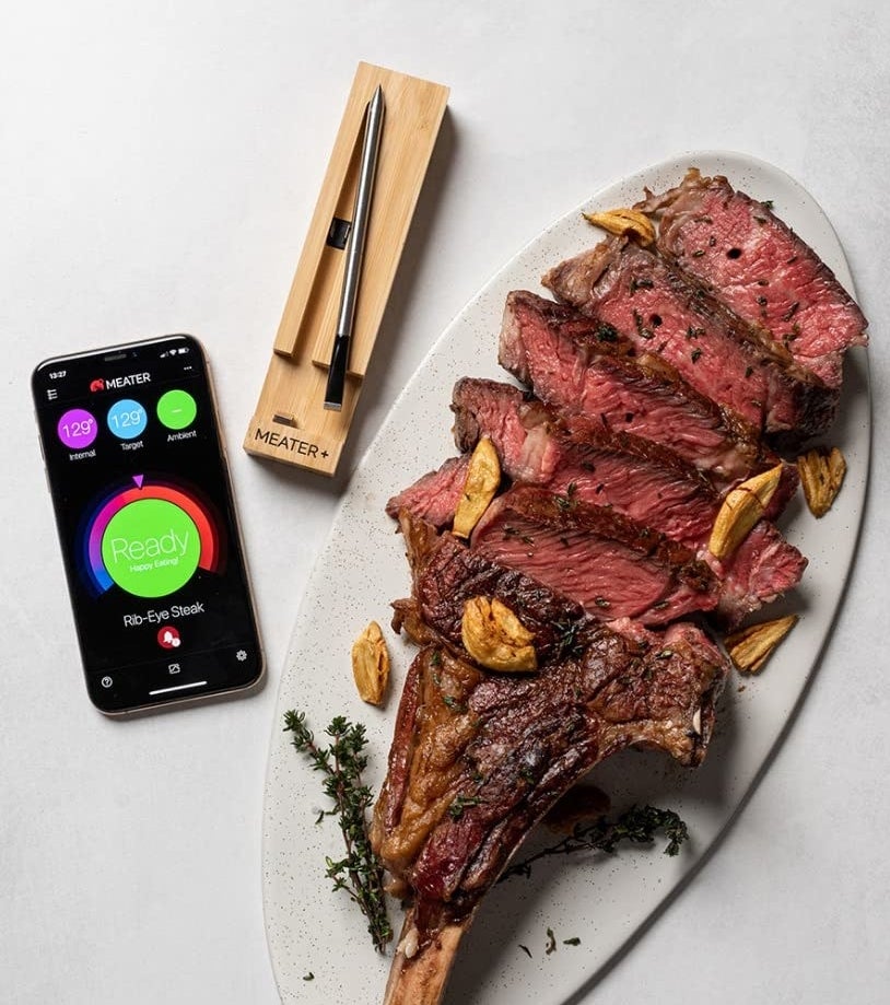 a large tomahawk steak next to the meat thermometer with the companion app open on a phone
