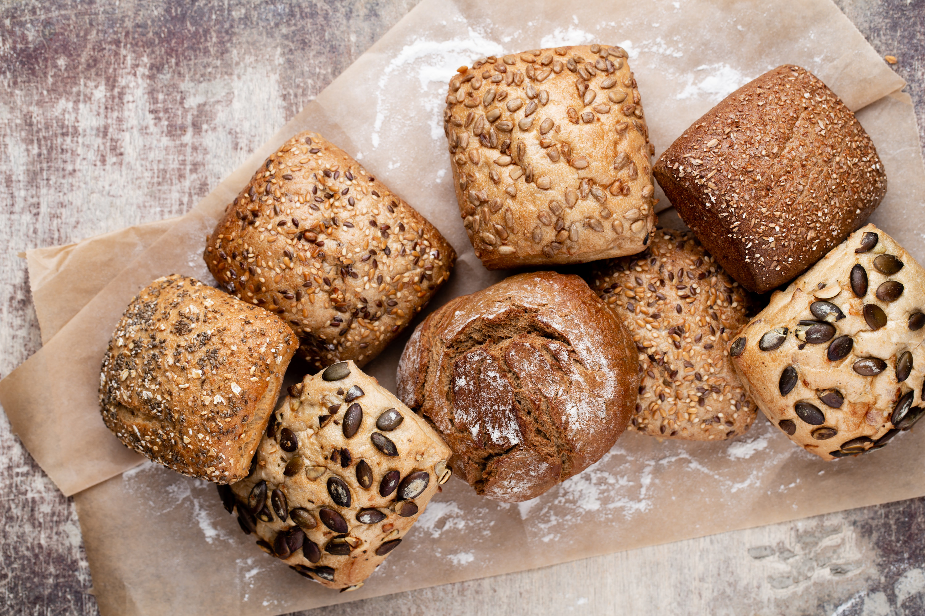 Eight rolls of various bread on top of brown paper bag