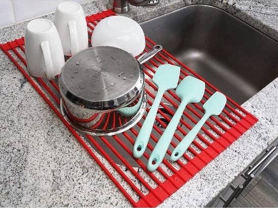 the red rack over half of the sink holding kitchen utensils, mugs, bowl and pan
