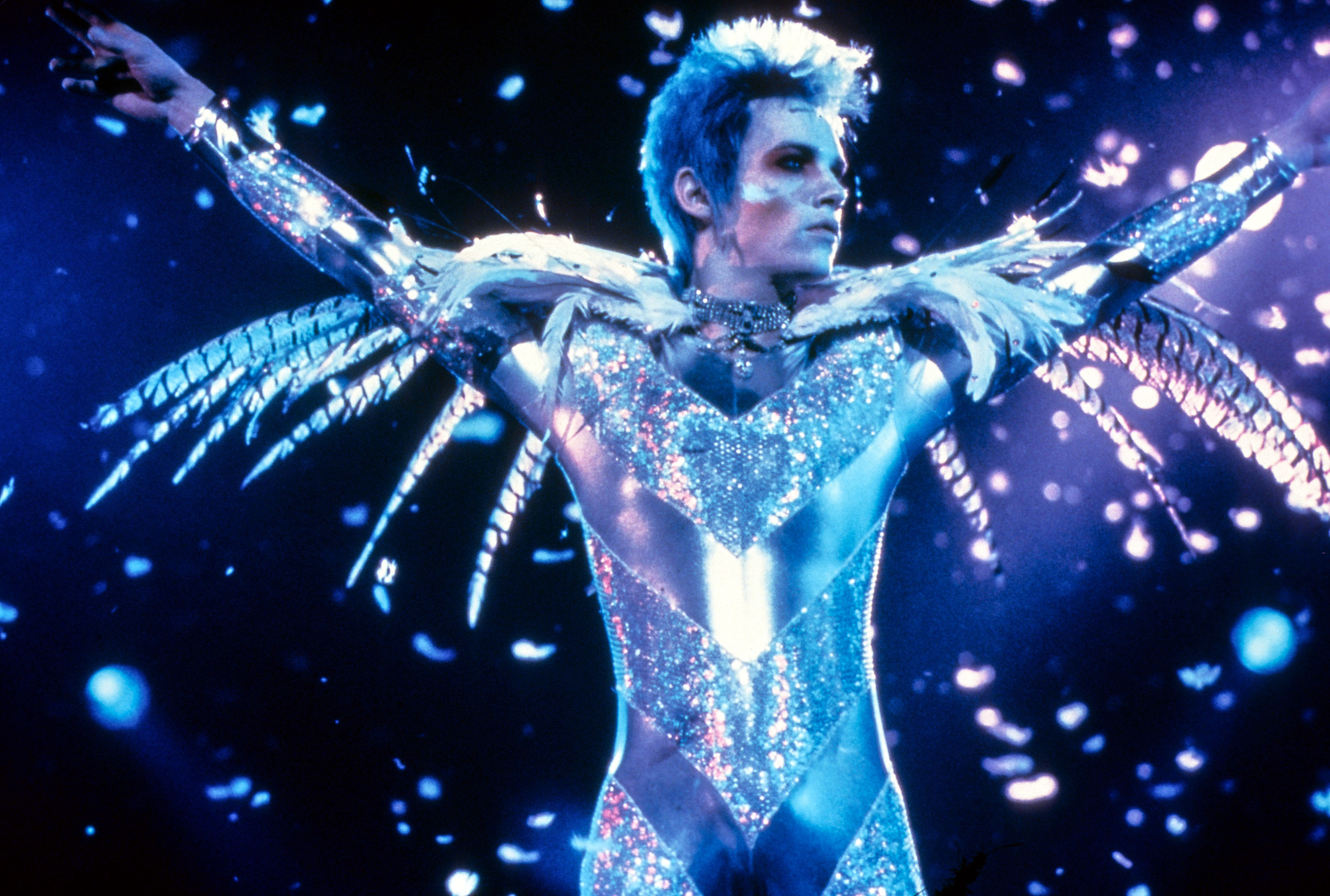 Jonathan Rhys-Myers as brian slade in velvet goldmine on stage in a silver jumpsuit with short blue hair and sideburns