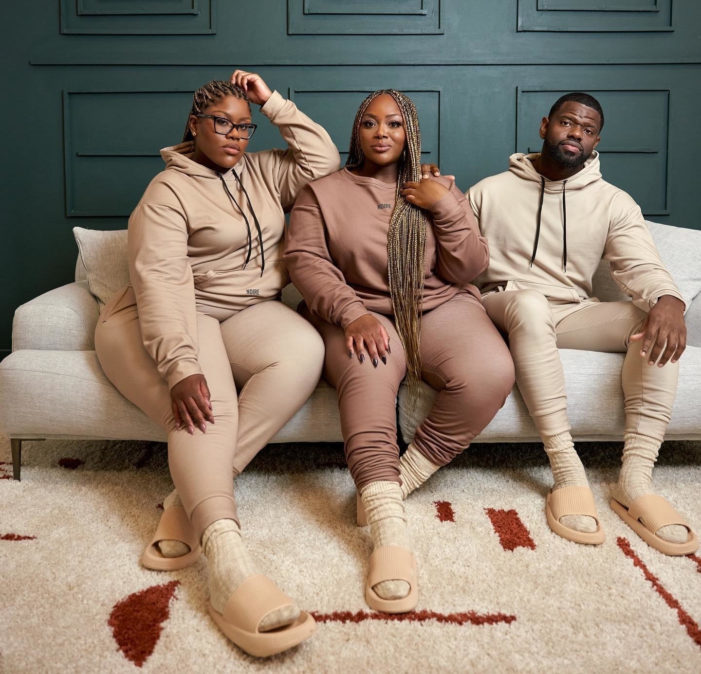 three models wearing different shades of nude hoodies, joggers, socks, and slides