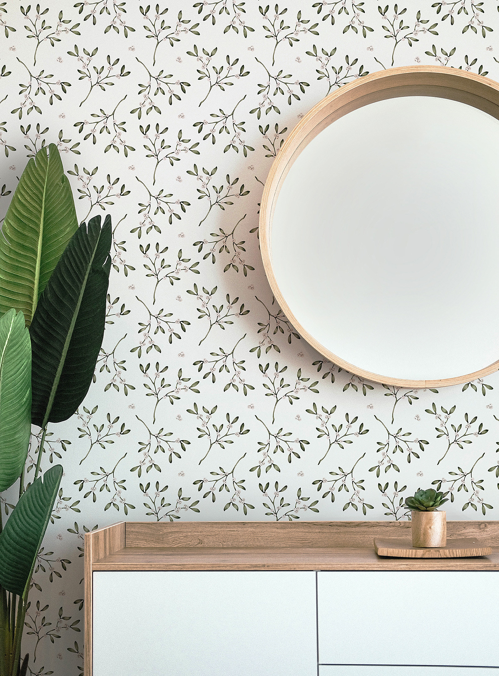 The wallpaper up on a wall behind a dresser, a plant, and a round mirror