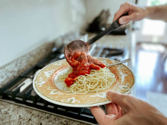 Man pouring sauce over spaghetti.