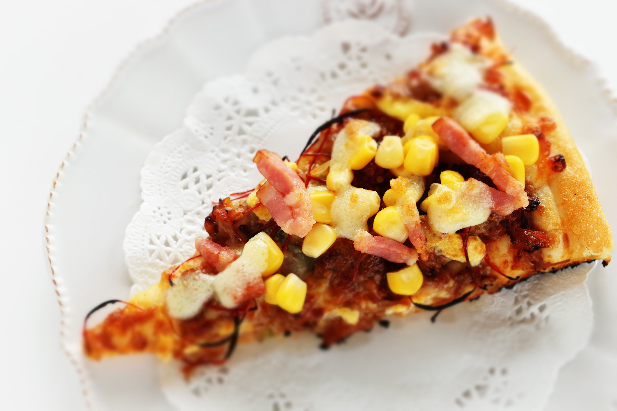 A slice of pizza topped with bacon and corn.