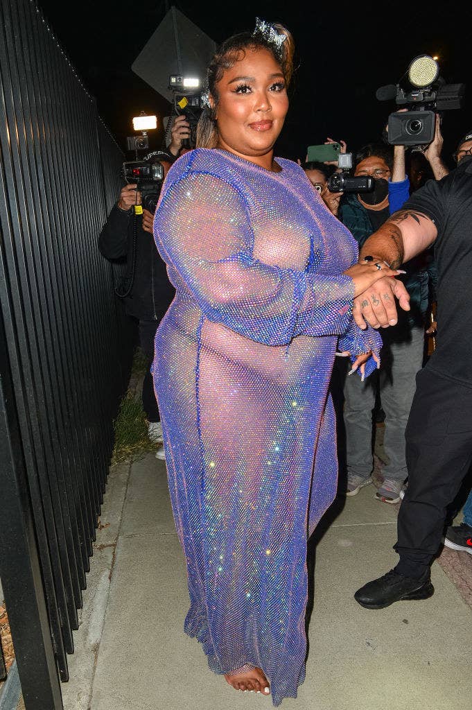 Lizzo getting her picture taken outside of a venue as she wears a sequined sheer dress