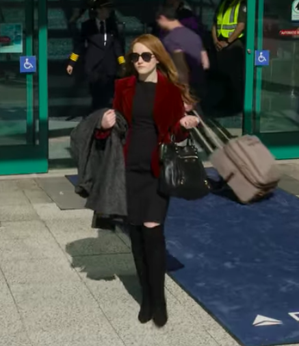 dressed in a bulky coat, plain dress, and thick glasses, Anna arrives in LA