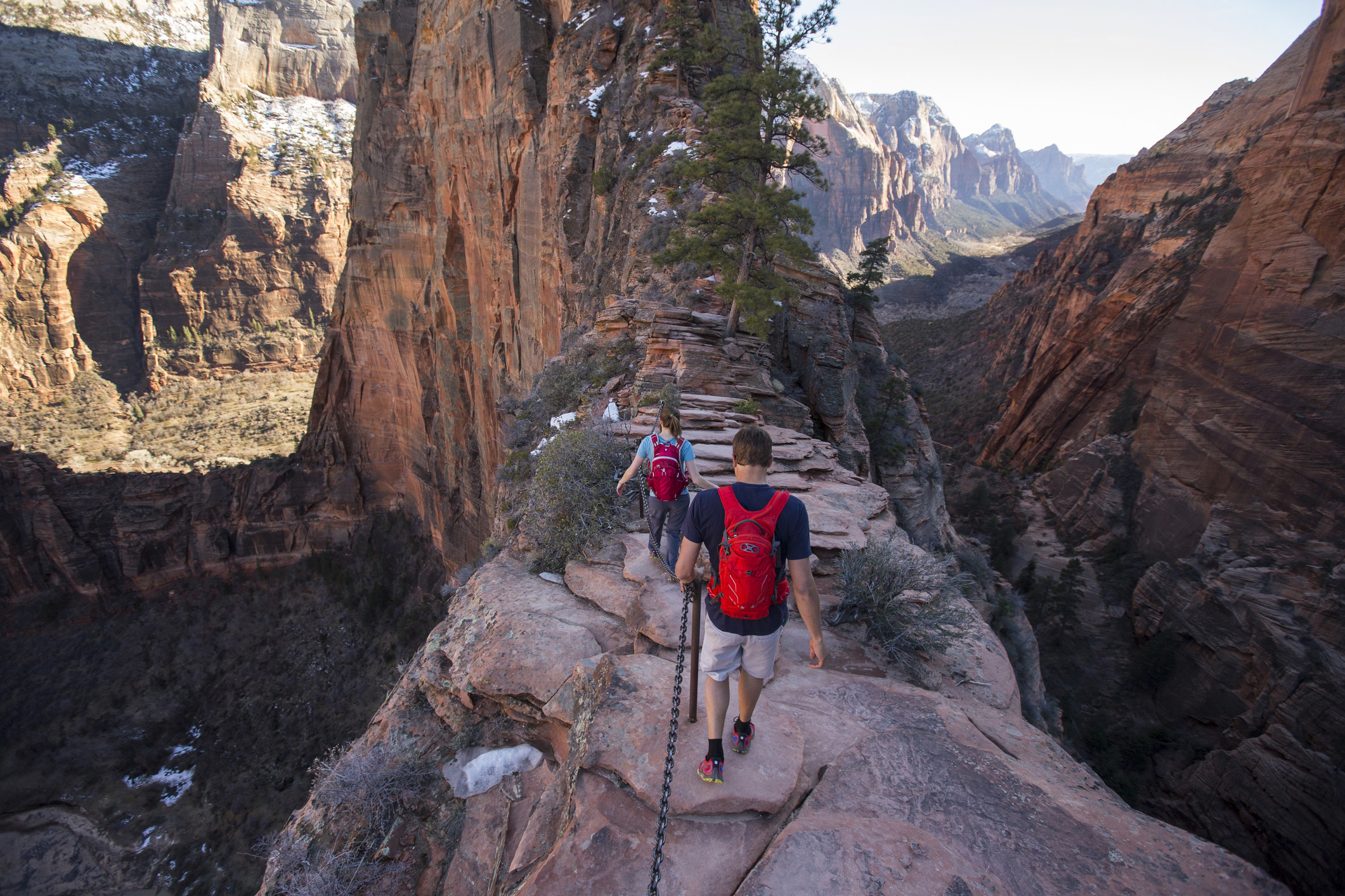 A pair of hikers walking along Angels Landing with a steep drop-off on either side in Zion National Park