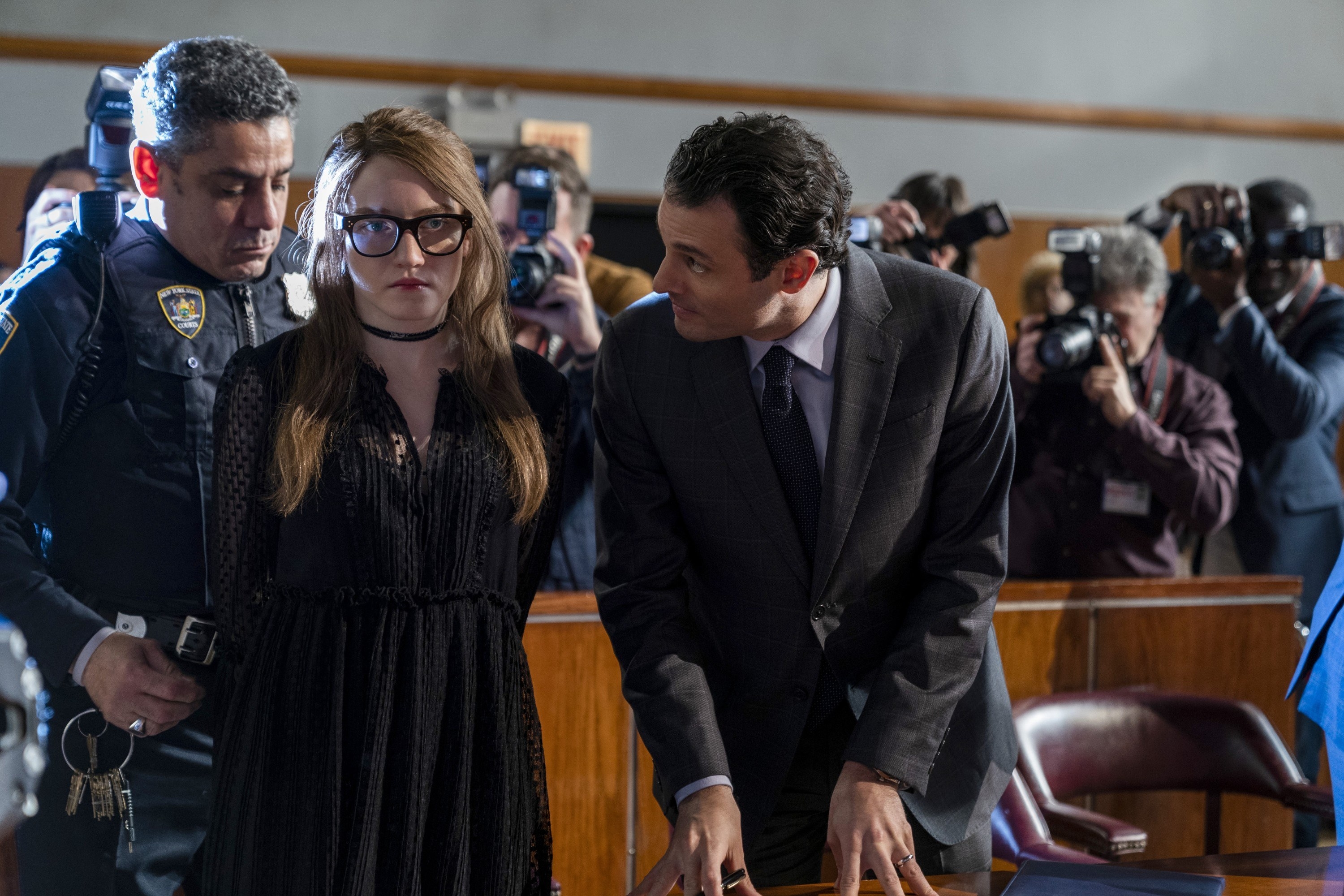 dressed in a long-sleeved babydoll dress, Anna is handcuffed in court