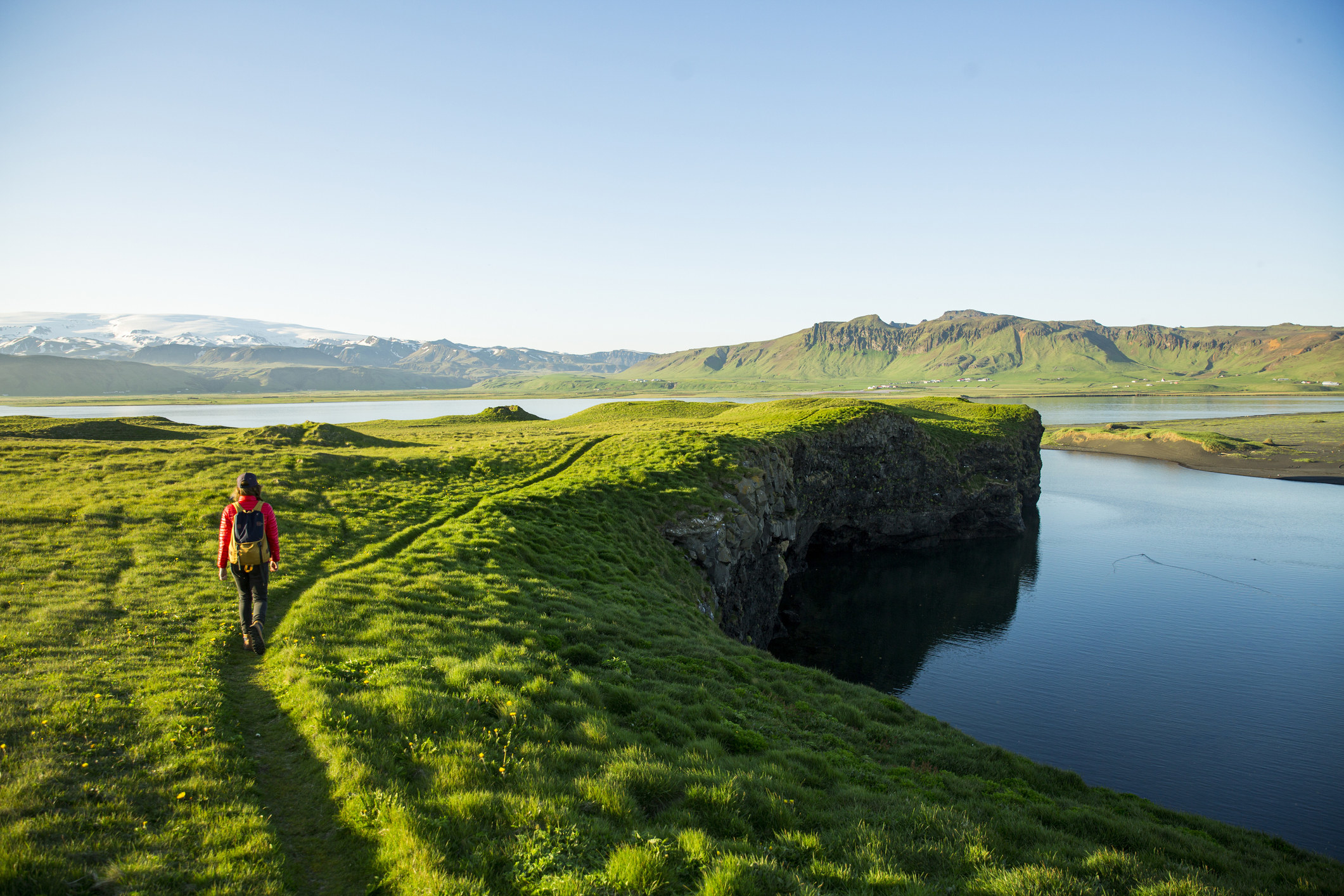 A hiker walking along a grassy path near a lagoon in Iceland