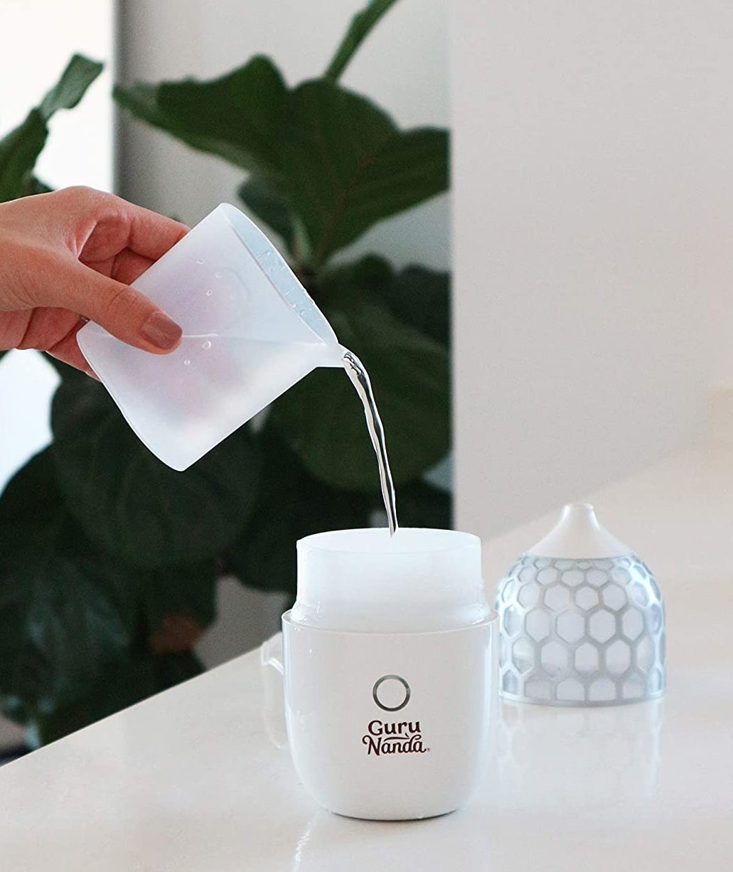 A person pouring water into their essential oil diffuser while it sits on a counter