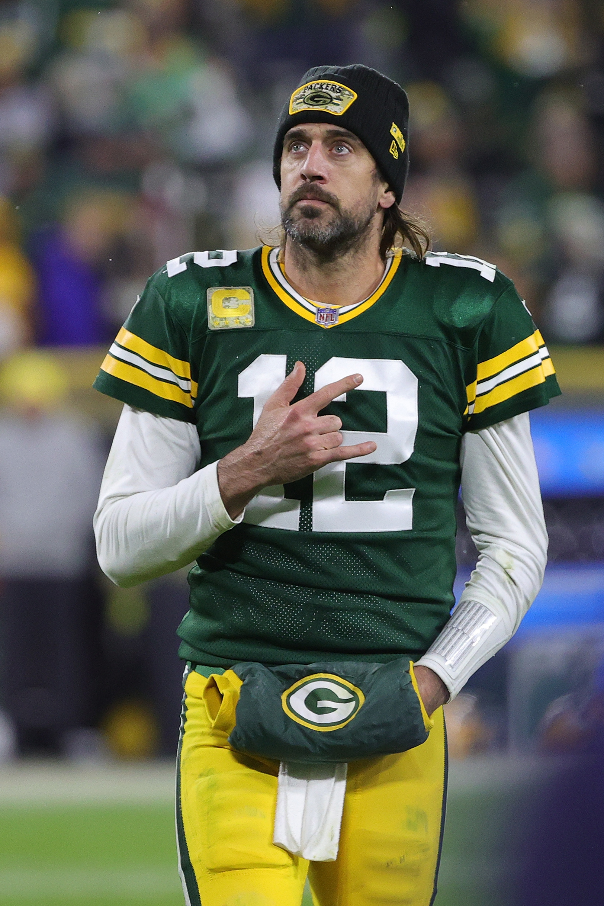 Rodgers makes a hand gesture while walking on the field in his uniform