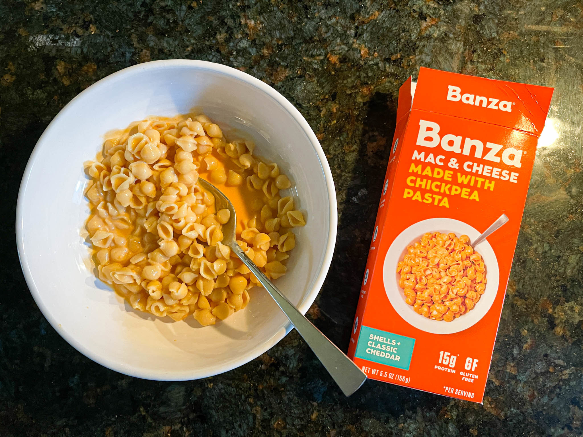 Cooked Banza mac n cheese in a bowl next to the packaging