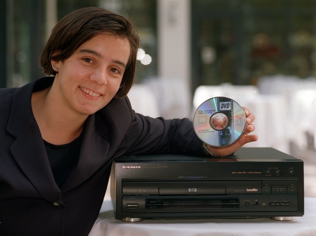 Young person holding a DVD while leaning against an early DVD player