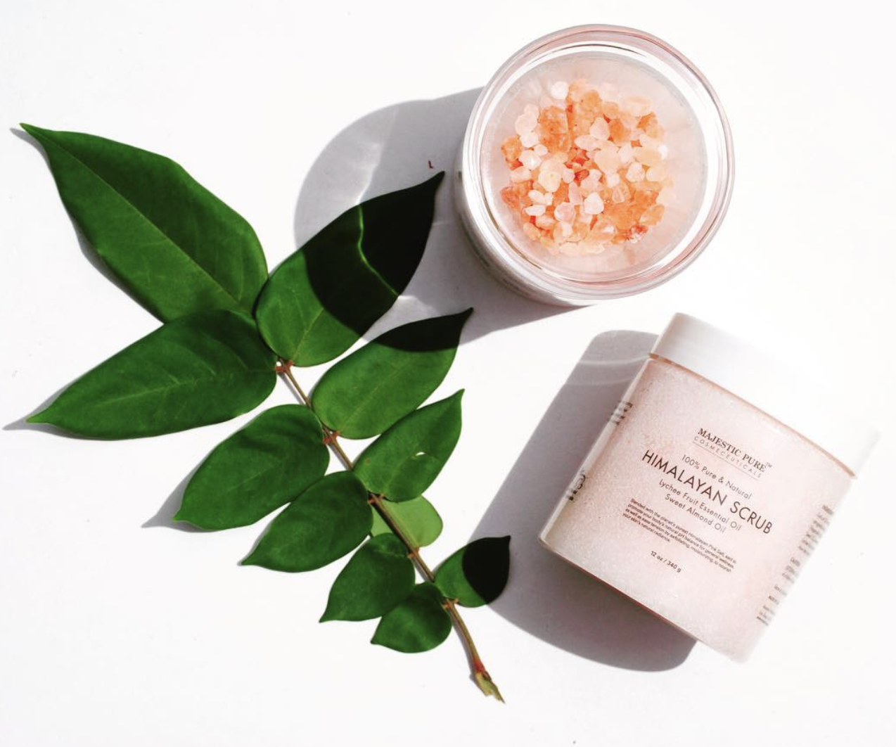 A tub of the salt scrub next to a plant leaf and a bowl of himalayan salt
