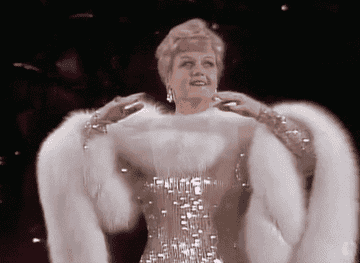 Gif of Angela Lansbury at the Oscars in a glittery champagne dress and white fur stole