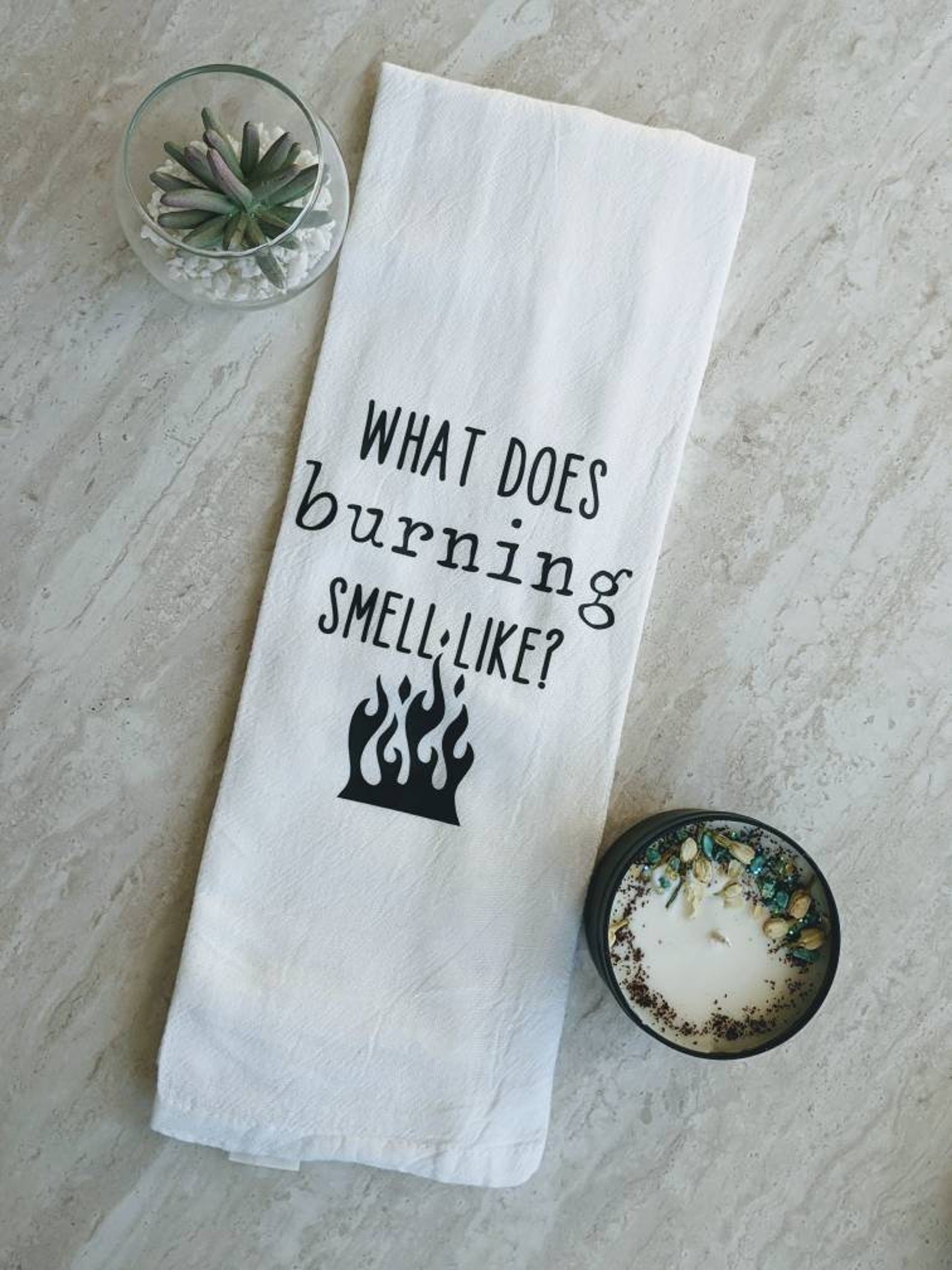 a white tea towel that says &quot;what does burning smell like?&quot; with a small flames icon