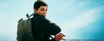 Logan Lerman waving his hand wildly and the sea becoming a wave to cover a big boat. Two other teen in sitting in a blow up boat watching.