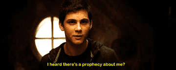 Logan Lerman as Percy Jackson standing in front of a circular window in a hoodie.