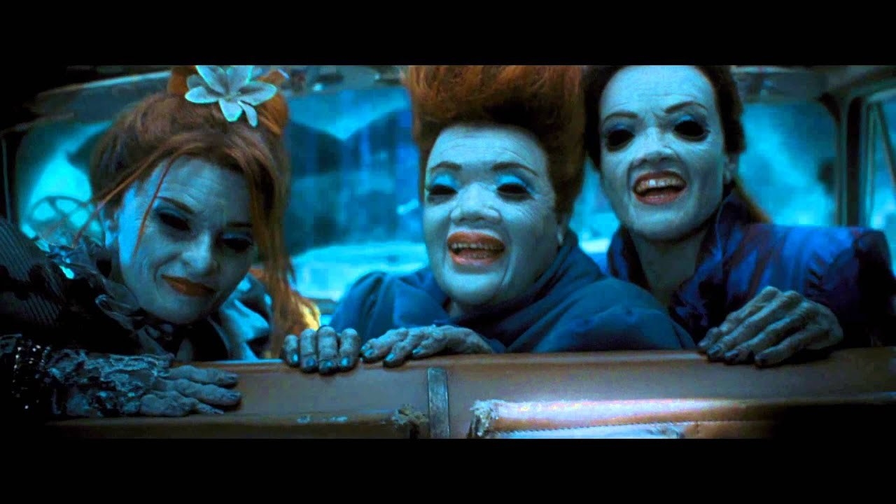 Three women with blue skin turned around to look behind them. They are all smiling, have ginger hair, old looking hands and bad teeth.