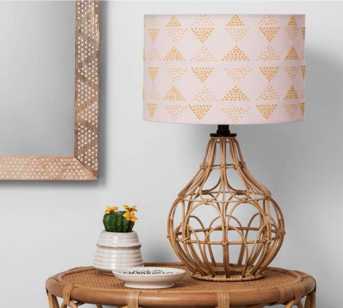A rattan table lamp with a pink and orange shade
