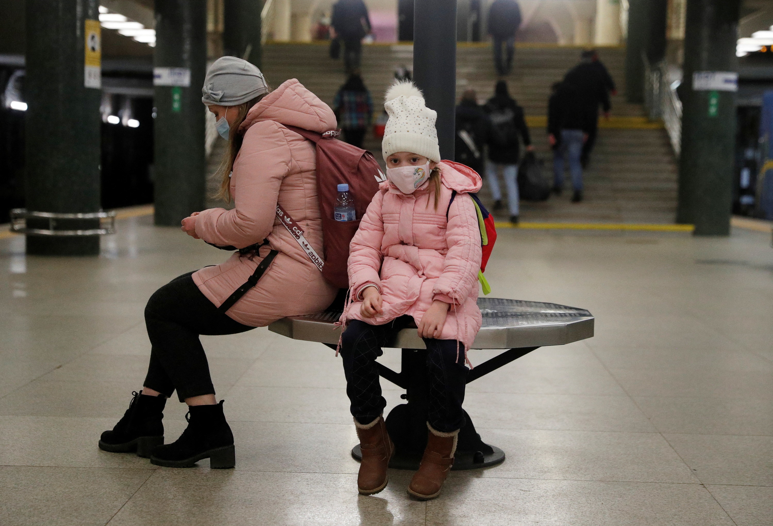 In the foreground, two people, one appearing to be a child, are sitting wearing backpacks