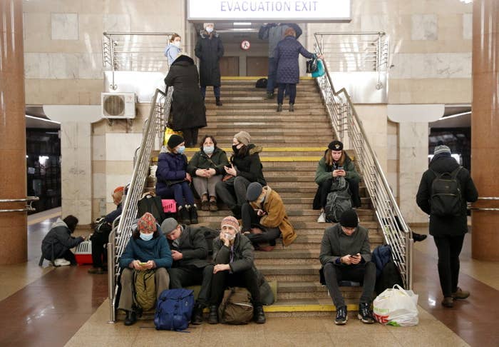 People in coats sitting on the steps of a subway station