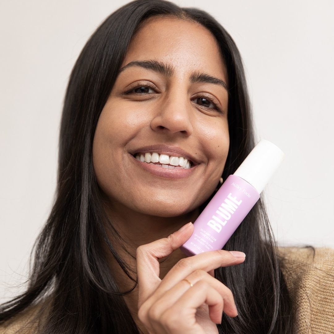 a smiling person holding a bottle of the serum while looking into the camera