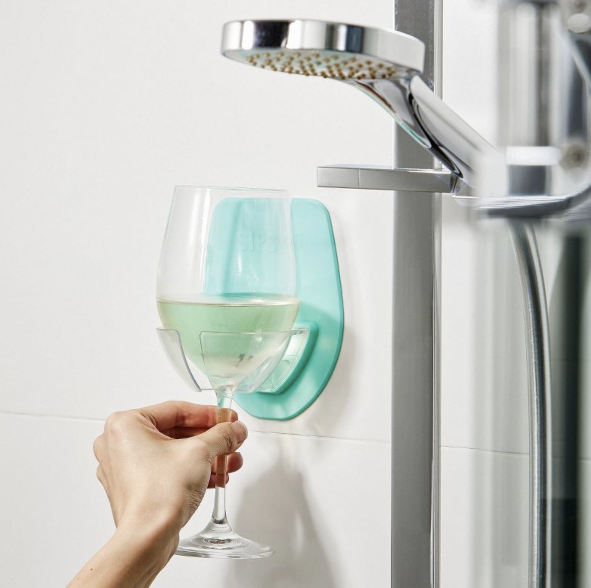 The teal wine holder adhered to side of shower and holding glass of white wine