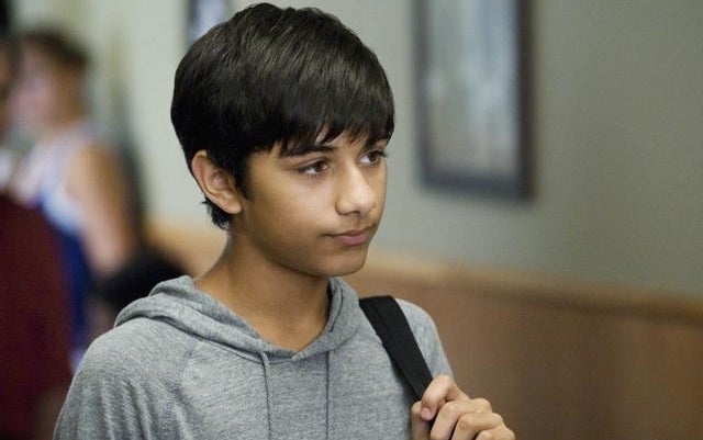 Mark Indelicato as "Justin" from Ugly Betty is pictured with a gray hoodie and backpack while he looks into the distance