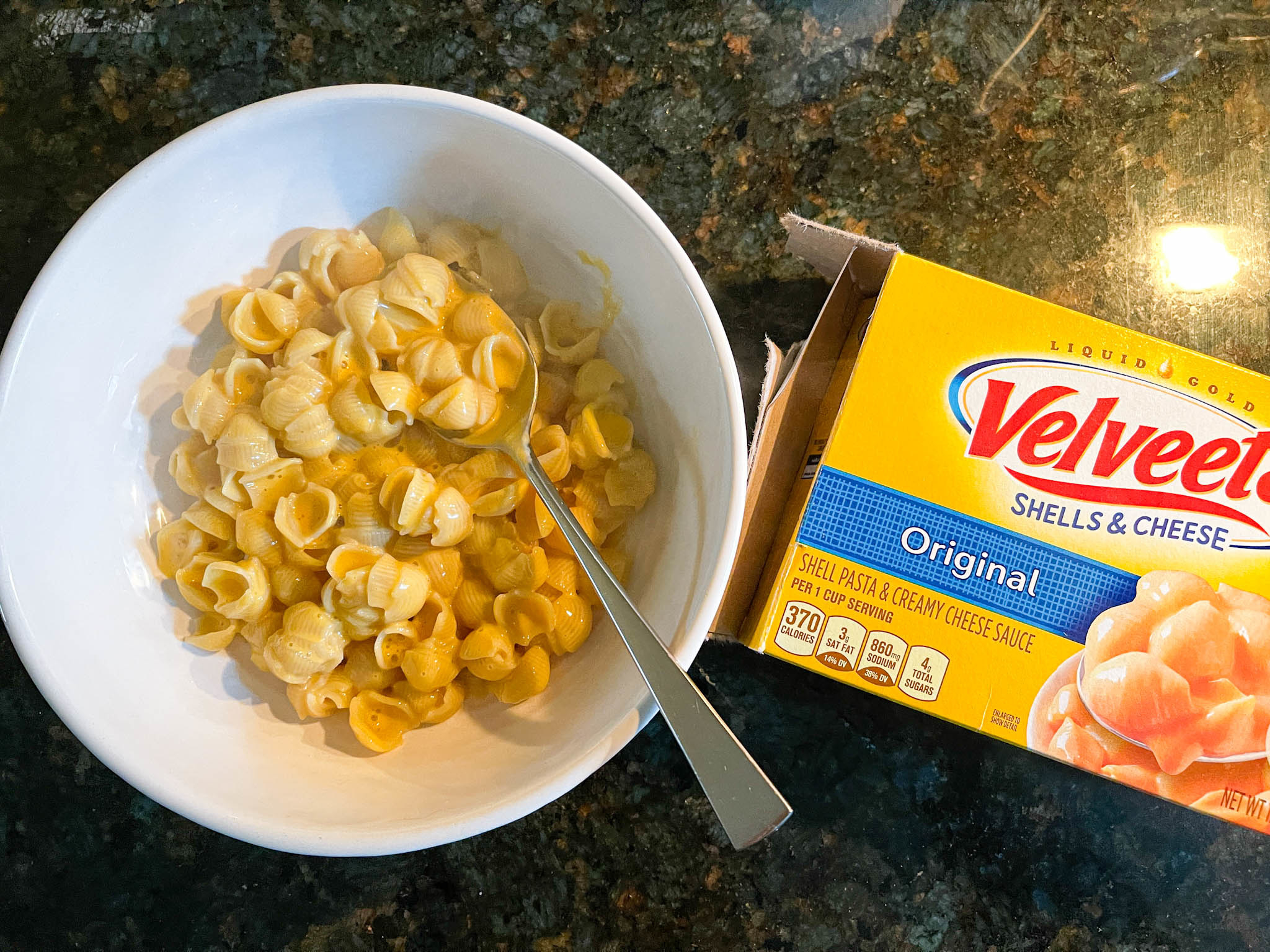 Cooked Velveeta mac &#x27;n&#x27; cheese in a bowl, next to its packaging
