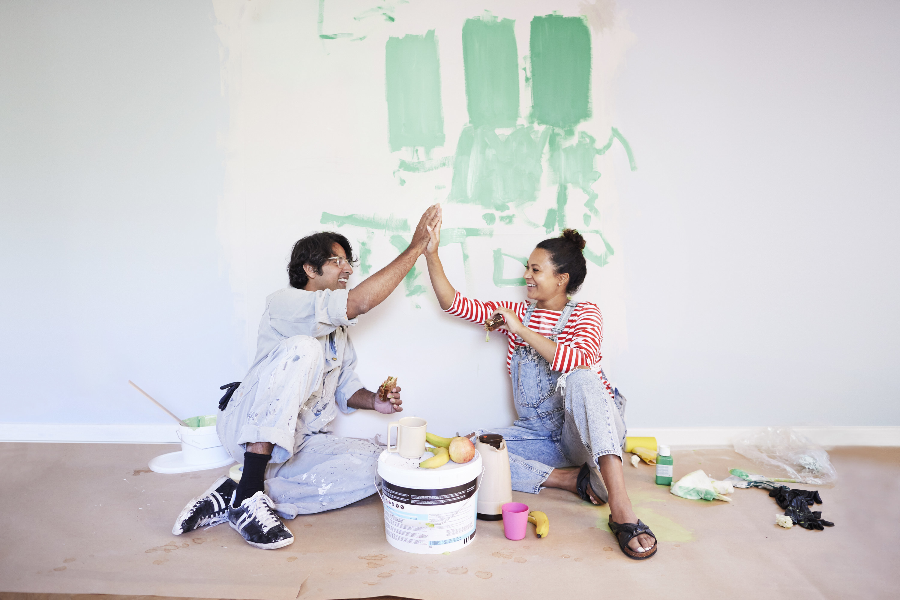 Young couple high-fiving while taking a break from painting their living room