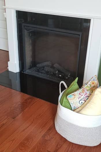 a reviewer photo of a wide basket filled with blanket sitting by a fireplace