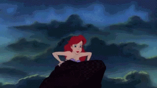 Princess Ariel sits on a rock as waves crash behind her