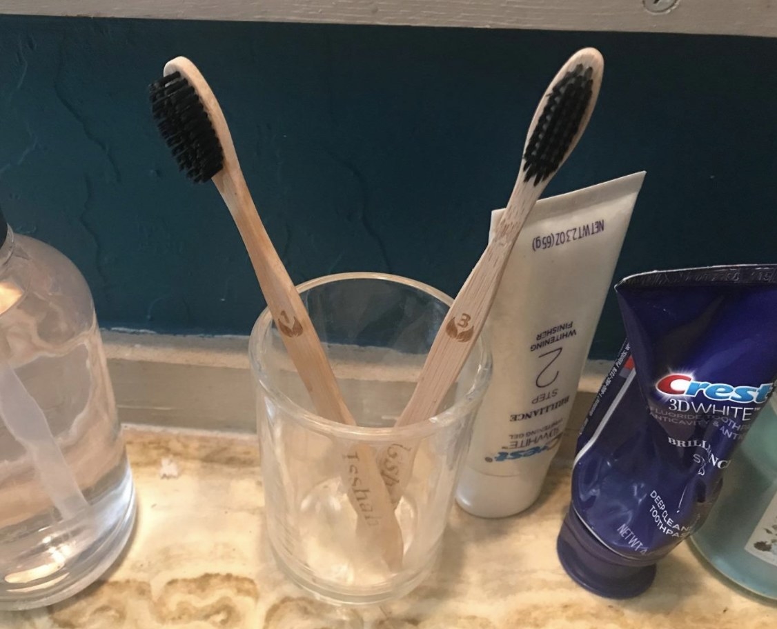 reviewer photo showing a glass on their bathroom vanity with two of the bamboo toothbrushes resting in it