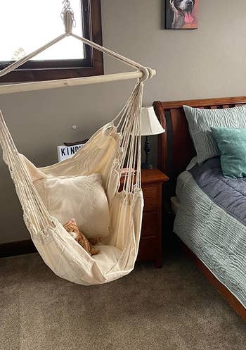 a reviewer photo of the hammock chair in tan hanging from the ceiling in a bedroom