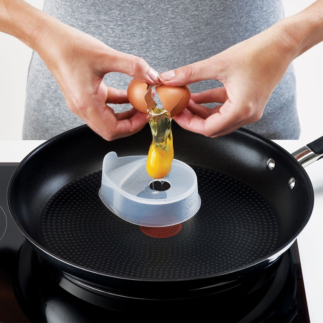a person cracking an egg into the poaching pods on a frying pan