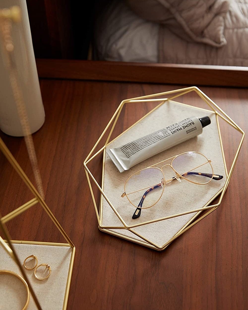 The trinket tray on a bedside table with a tube of cream and a pair of glasses placed inside