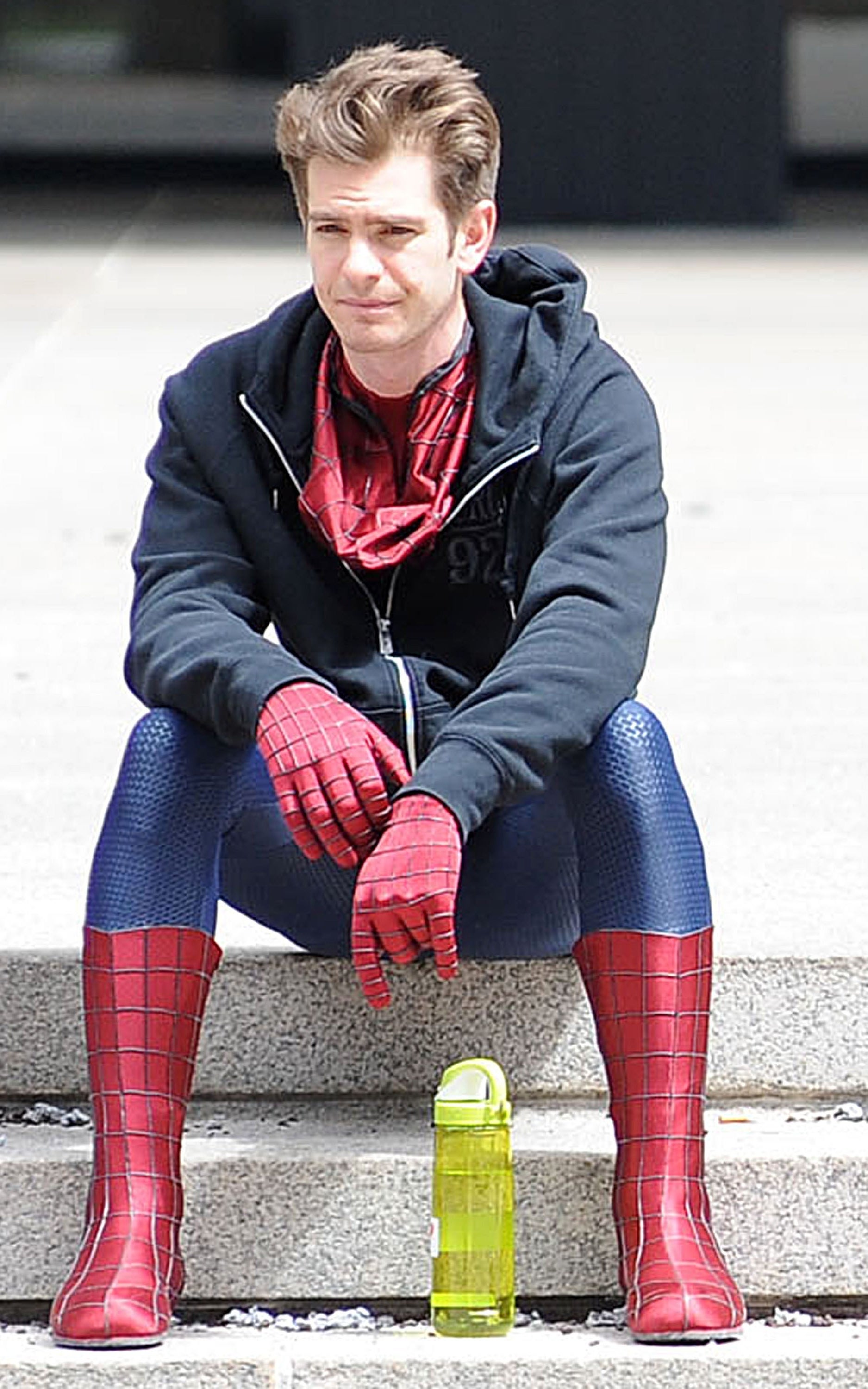 wearing a hoodie over his Spidey suit, Peter sits on the sidewalk