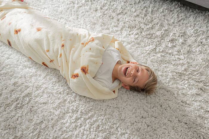 A child rolled up in the blanket as they lay on the floor